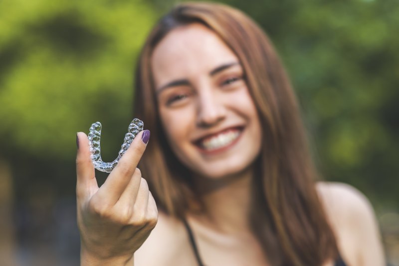 person holding up Invisalign retainer and smiling